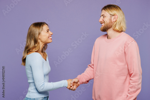 Side profile view smiling fun young couple two friends family man woman wear pink blue casual clothes together do hand shake gesture isolated on pastel plain light purple background studio portrait.