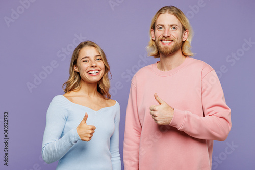 Young smiling satisfied happy couple two friends family man woman wear pink blue casual clothes together showing thumb up like gesture isolated on pastel plain light purple background studio portrait.