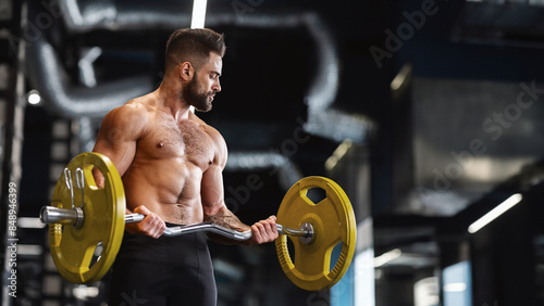 Handsome naked weightlifter lifting heavy barbell in gym, free space