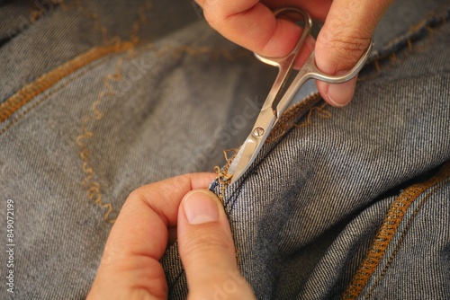 A woman hands with scissors cutting open the seam on a jeans dress