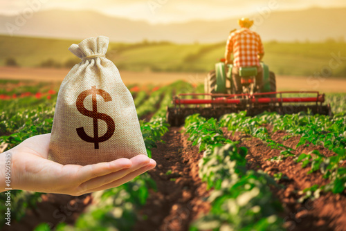 Hand with a dollar money bag on the background of a farm field with a farmer on a tractor. Investments in agriculture and agribusiness. Subsidies support for agricultural producers. Land market