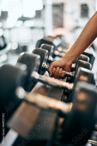 Close-up photo of a female hand picking up a heavy dumbbell, at the gym.
