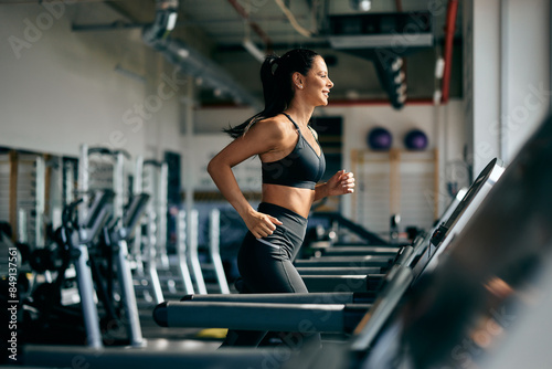 Side profile of a smiling fit woman running on a treadmill at the gym.