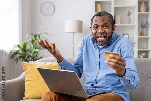 A confused man holding a credit card while shopping online, displaying concern about potential internet fraud and online scams.