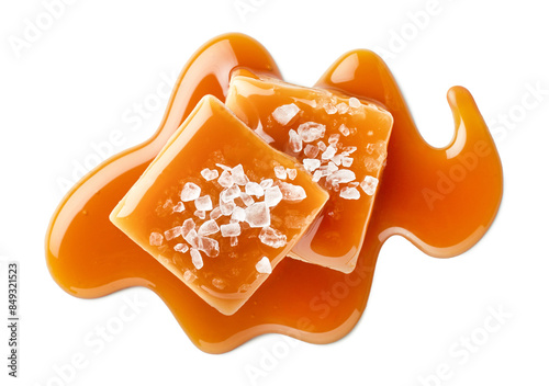 Two salty or salted caramel candy cubes topped with caramel sauce and sea salt on white background