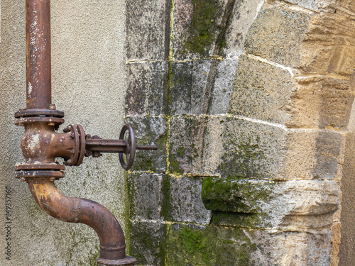 An old pipeline running outside the old building. Pipes with fittings on the background of ancient masonry of an ancient wall. A valve shutting off the water supply.