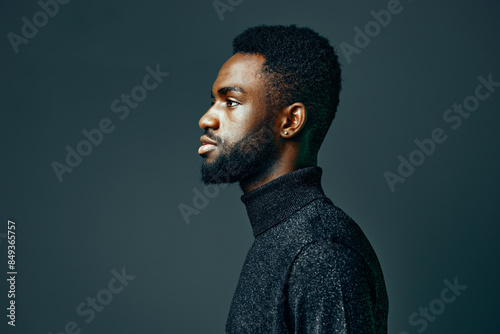 Confident young african american man with beard in a turtleneck, gazing thoughtfully against a dark background