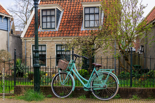 A mint green ladies' bicycle with a cargo basket stands against a wrought-iron garden fence in the Dutch town of Edam