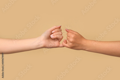 Women making pinky promise on color background, closeup. Friendship Day celebration