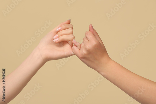 Women making pinky promise on color background, closeup. Friendship Day celebration