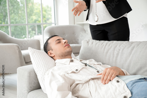 Female psychologist with pocket watch hypnotizing young man in office