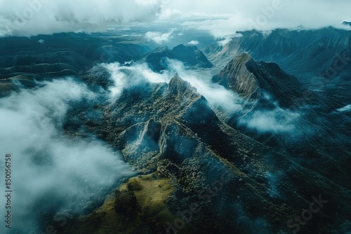 Aerial view of majestic mountain range shrouded in clouds, revealing dramatic peaks and lush valleys.