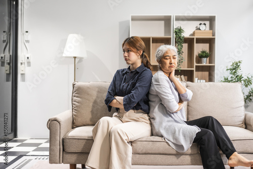 A mature mom and her young daughter, both Asian, sit on a sofa, engaged in a quarrel. Their argument escalates into a conflict, with clashes and friction over misunderstandings.