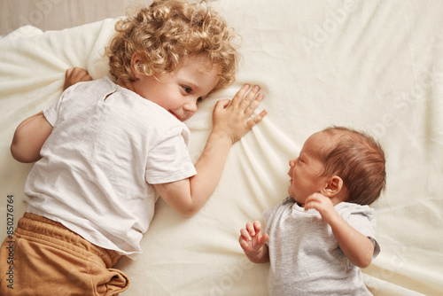 Happy toddler with her brother. Caucasian siblings at home. Cute brother and sister moments. Curious wavy haired older sister with newborn baby