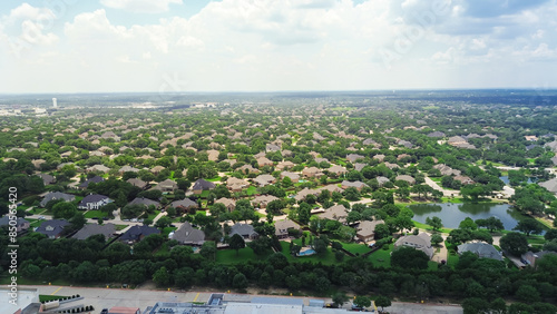 Urban sprawl with row of upscale two-story suburban home in large lot backyard, local pond with water fountain in master planned community water tower in distant background, Southlake, Texas