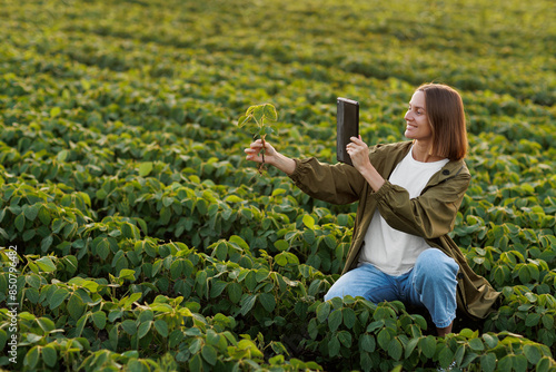 Smart farming soybean technology. Smiling female farmer with digital tablet uses for examine and check soya plants in field. Modern agribusiness of control of growth and development of sprouts