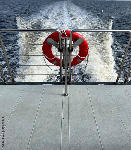 Wake of water behind a boat with railings and lifebuoy .