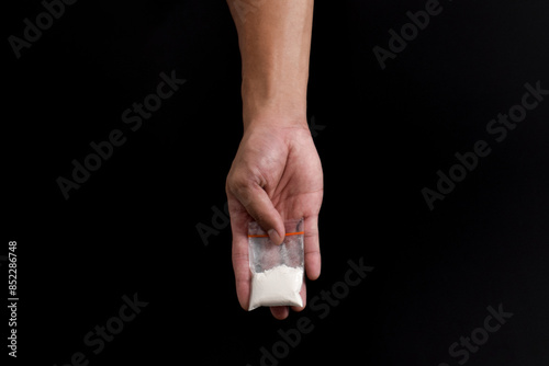 Hand giving cocaine in plastic package isolated on black background. Illustration of illegal drug substances, narcotics