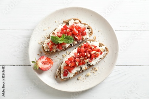 Bruschettas with ricotta cheese, chopped strawberries and mint on white wooden table, top view