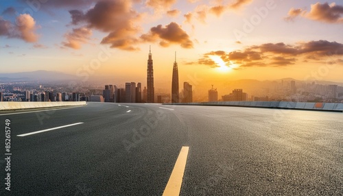 An empty asphalt road extends into a modern city skyline at sunset, offering a high-angle