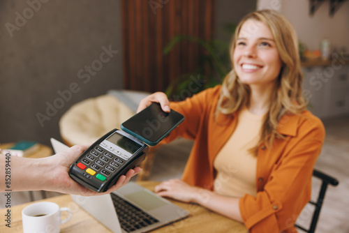 Young woman wear shirt hold bank payment terminal process acquire mobile cell phone pay bill sit alone at table in coffee shop cafe relax rest at restaurant inside. Freelance office business concept.