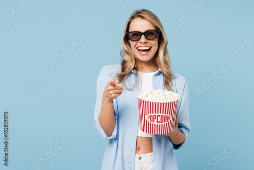 Young cool woman she wears white top shirt casual clothes 3d glasses watch movie film hold bucket of popcorn in cinema point finger camera on you isolated on plain pastel light blue cyan background .