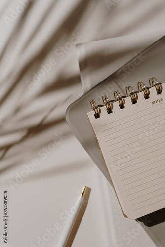 Top view of notebook with blank sheet on white background with aesthetic floral palm leaves sunlight shadows. Flat lay mockup with copy space