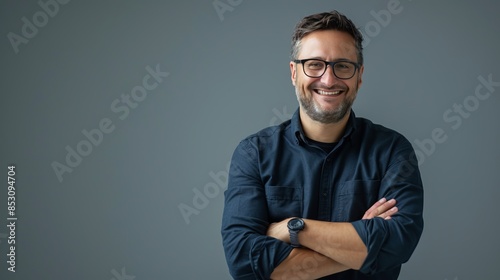 Portrait of a smiling man with glasses and beard, against a plain background. Casual clothing style with folded arms. Suitable for presentations, marketing and professional use. AI