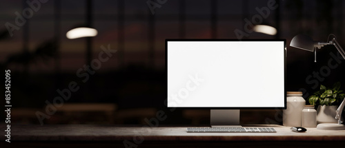 A computer mockup, decor, and a dim light from a lamp on a table in a dark office room at night.