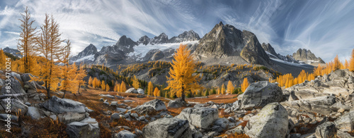 A panoramic view of the Kootenay mountain range in British Columbia, Canada with yellow larch trees and green pines dotting its slopes. 