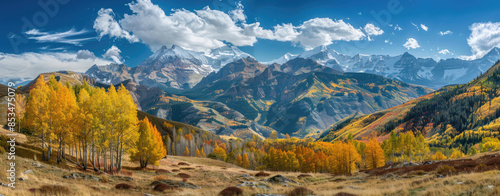 A panoramic view of the Kootenay mountain range in British Columbia, Canada with yellow larch trees and green pines dotting its slopes. 