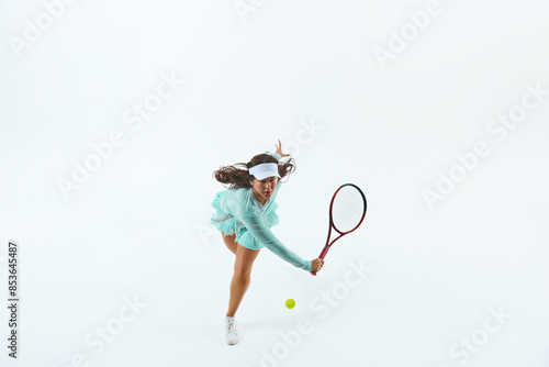 Athletic female tennis player in light blue sports attire strikes forehand shot against white studio background. Concept of professional sport, championship, active lifestyle, tournament. Ad