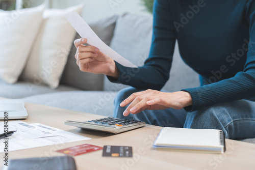 Stressed asian young business woman, employee using calculator to calculate expenses of monthly, hand holding bills and receipt for to payment on table at home. Financial, finance of banking concept.