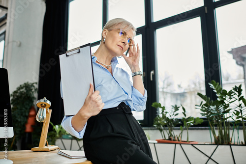 Middle aged businesswoman with short hair seated at office desk, feeling unwell during menopause