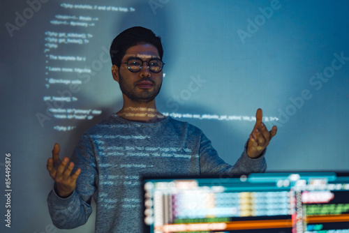 Indian man programmer standing in front of a screen with code projected presentation the integration of technology and human expertise in software development