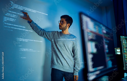 Indian man programmer standing in front of a screen with code projected presentation the integration of technology and human expertise in software development