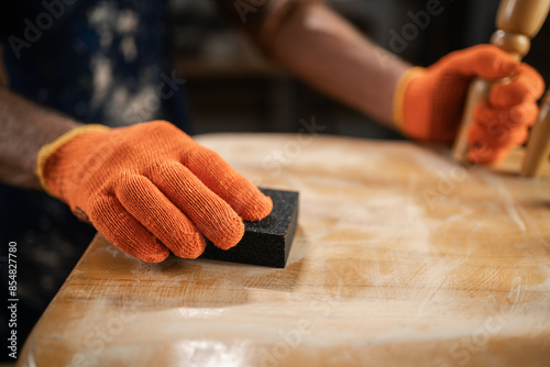 furniture repair, DIY and home improvement concept. man in orange gloves sanding wooden chair with sandpaper, preparing surface for further processing.