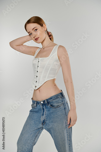 A young woman wearing a white corset poses against a white backdrop.