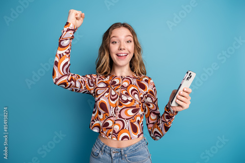 Photo of nice young girl hold phone raise fist wear top isolated on blue color background