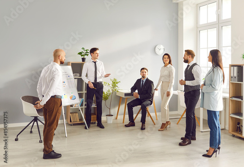 Group of business people chatting on a meeting standing in circle in office. Company employees discussing work project. Coworkers listen to their colleague. Corporate business team concept.