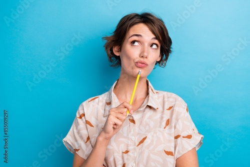 Photo of creative pensive lady hold pencil touch chin look interested empty space isolated on blue color background