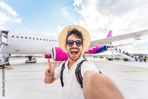 Happy tourist boarding on a plane at the airport - Handsome young man taking selfie picture in front of airplane - Summertime holidays and transportation life style concept