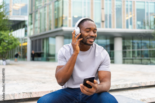 Music song concept. Good start day. Happy African American man listening modern hit on street in city. Person guy wearing headphones enjoy listening favorite music on phone. People lifestyle joy