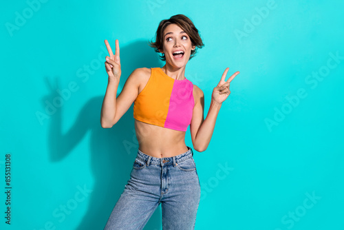 Photo of confident excited lady dressed colorful top showing two v-signs looking empty space isolated turquoise color background