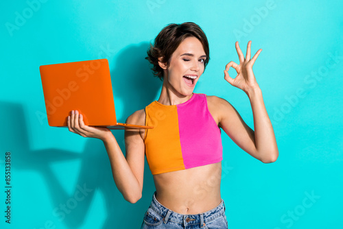 Photo of pretty flirty lady dressed colorful top working modern device winking showing okey isolated turquoise color background
