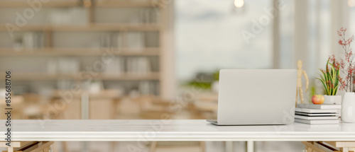 A laptop on a white tabletop in a minimalist coffee shop indoor seating area or co-working space.