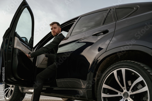 Man in black suit is sitting in the car, opening the door