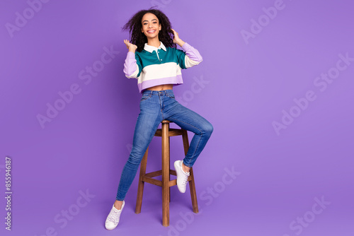 Full body portrait of lovely young girl sit stool touch hair wear shirt isolated on purple color background