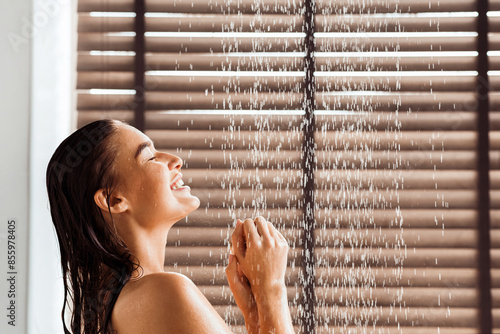 Young woman taking refreshing shower, standing under water drops, side view