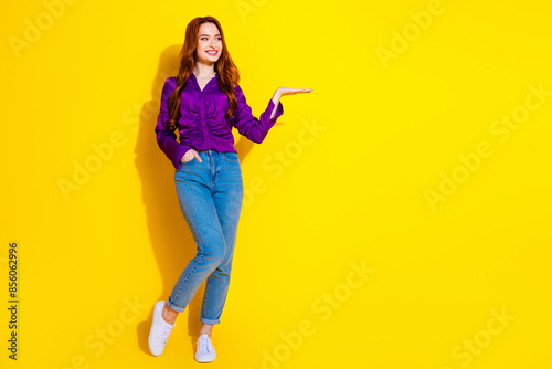 Full body length photo of red hair young woman in purple shirt and jeans advertising product weight empty space isolated on yellow color background